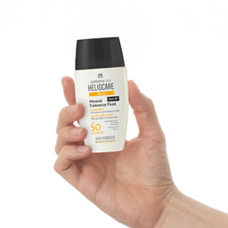 Hand holding a Heliocare sunscreen bottle against a white background