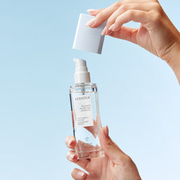Person holding a clear skincare bottle with a blue background