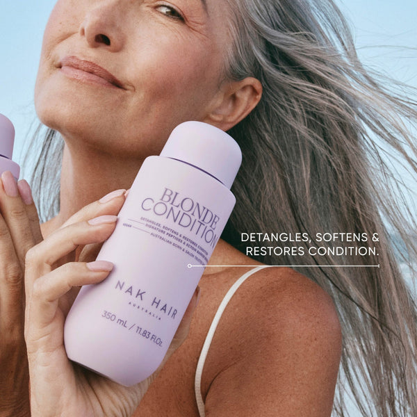 Woman holding a bottle of NAK Hair Blonde Conditioner with text on a light background
