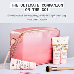 A pink metallic zip cosmetic bag with rose-gold hardware, shown with matching pink and white toiletry products and makeup brushes on a light gray surface. Text at the top reads 'THE ULTIMATE COMPANION ON THE GO!' and describes wipe-clean material and multi-use bag functionality.