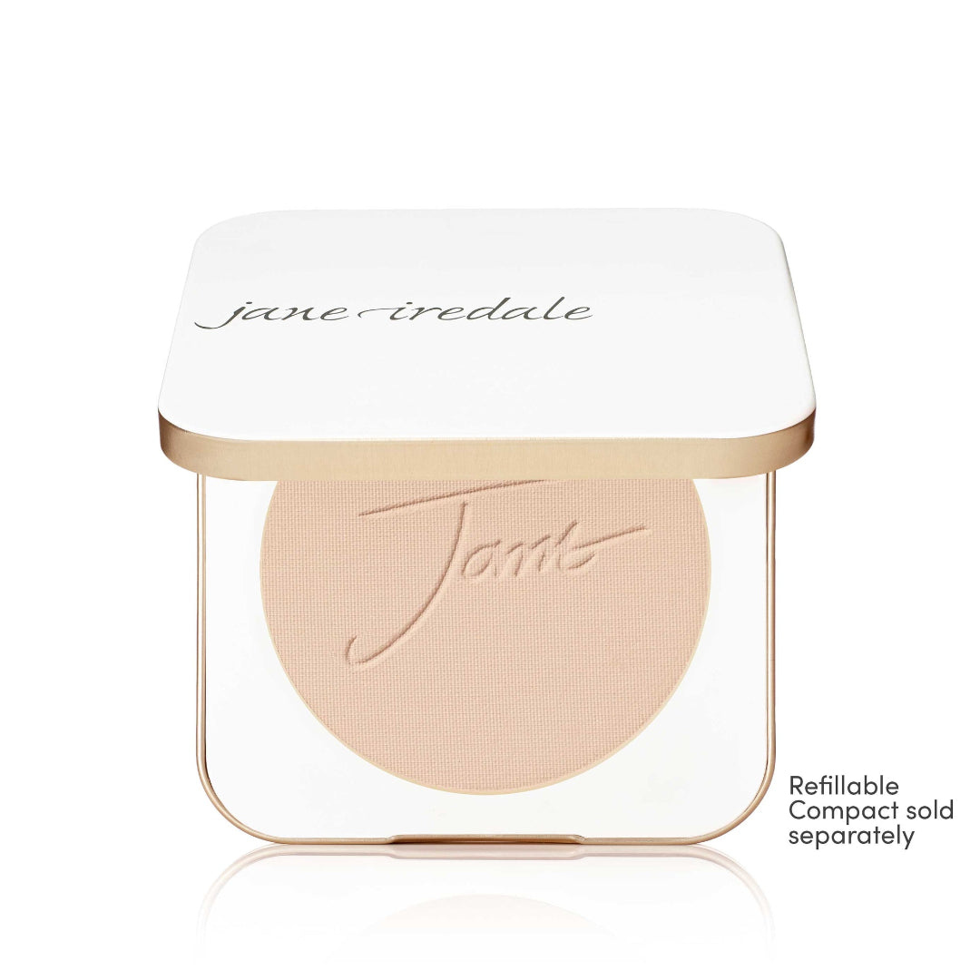 A Jane Iredale makeup compact with a white lid and a clear base showing a round blush or pressed powder in a light peach-beige shade. The compact has a thin metallic gold frame.