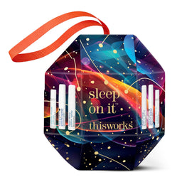 A hexagonal gift box with a bright orange ribbon handle, featuring a colorful cosmic design with the text 'sleep on it thisworks' and several small white spray bottles arranged on the front, set against a plain white background.