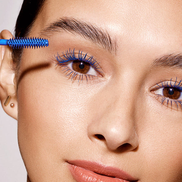 Close-up of a person applying mascara with a blue brush on a neutral background