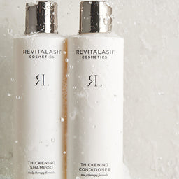 Two Revitalash Cosmetics bottles on a glass surface with water droplets.