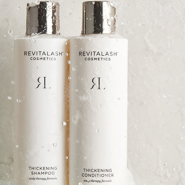 Two Revitalash Cosmetics bottles on a glass surface with water droplets.