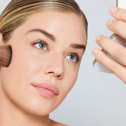 Woman applying makeup with a brush on a light gray background