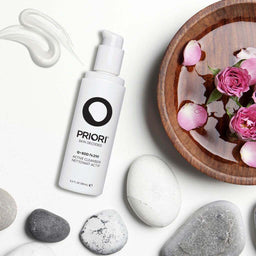 a bottle of PRIORI Q+SOD - Active Cleanser next to a bowl of flower petals and stones