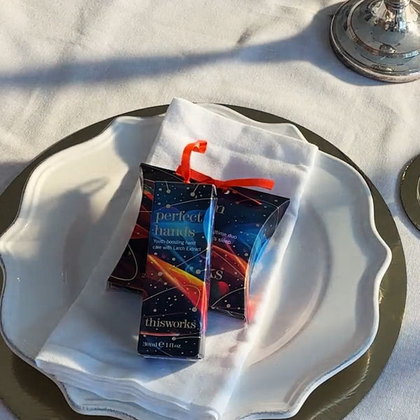 Two small boxed hand products labeled 'perfect hands' and 'thisworks' tied with red ribbons, placed on a white napkin over a white plate on a table with a white cloth background.