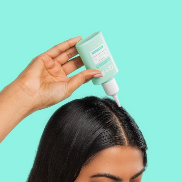 Person applying a green hair product to their hair against a teal background