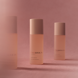 Three Omorovicza Capsule skincare bottles with pale peach-pink liquid and beige caps, arranged on a soft pink background with a central bottle in sharp focus and blurred bottles on either side.