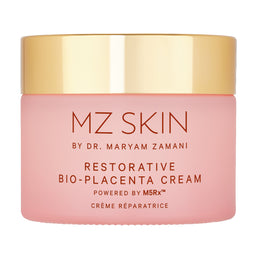 A pink cosmetic cream jar with a shiny gold lid, labeled 'MZ SKIN BY DR. MARYAM ZAMANI RESTORATIVE BIO-PLACENTA CREAM'.