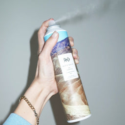 a can of R+Co Death Valley Dry Shampoo being sprayed into the air