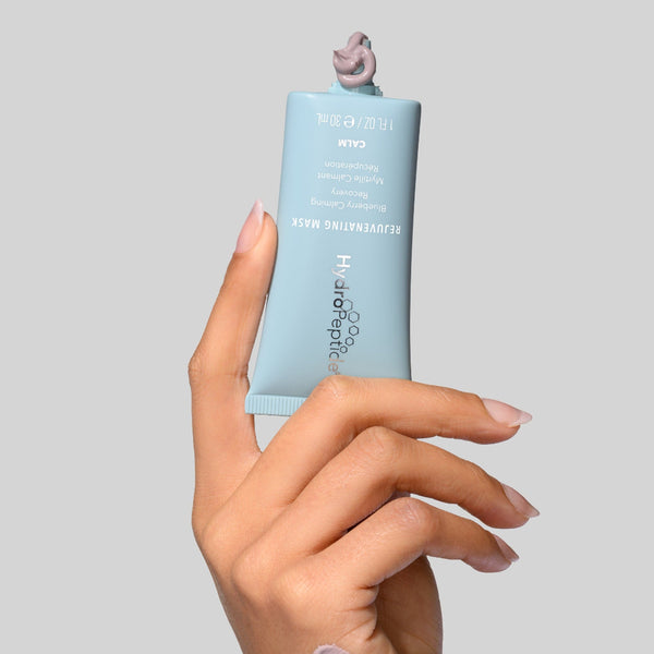 Hand holding a tube of skincare product against a gray background