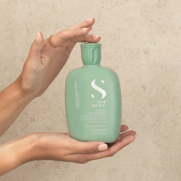 Person holding a green bottle of Alfaparf Milano styling product against a beige background