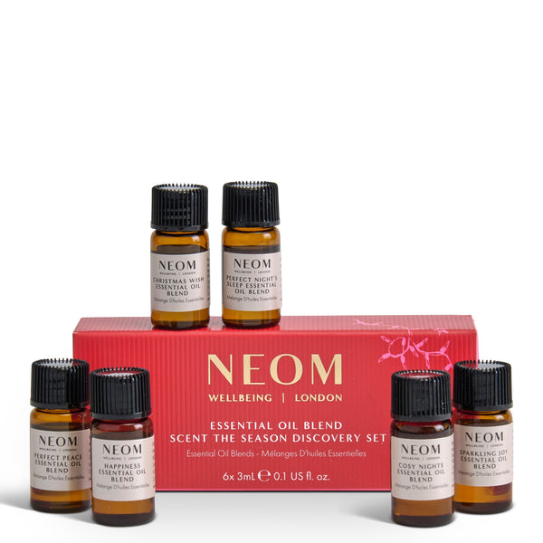 NEOM Wellbeing London Scent the Season Discovery Set, featuring a red gift box and six amber glass essential oil bottles with black caps and cream labels, arranged on a white background.