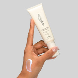 Hand holding a tube of skincare product with a gray background