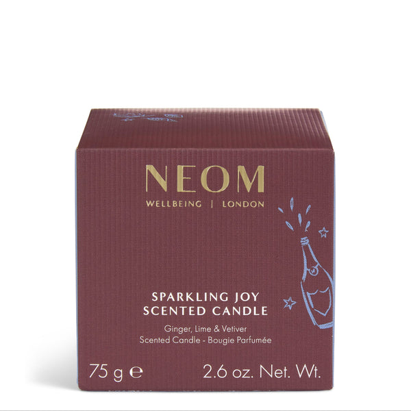 A square NEOM Wellbeing London 'Sparkling Joy' scented candle box in a deep burgundy color with gold lettering and a light blue champagne bottle illustration, set against a plain white background.