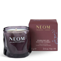 A NEOM Wellbeing London Sparkling Joy scented candle in a dark purple glass jar, shown next to its matching dark burgundy box on a clean white background.