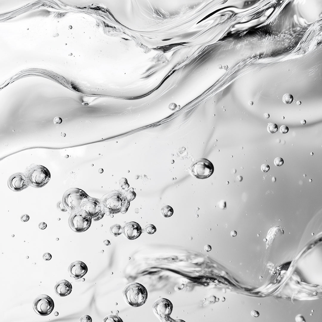 Abstract close-up of clear liquid with flowing ripples and scattered transparent bubbles in a monochrome gray-white composition.