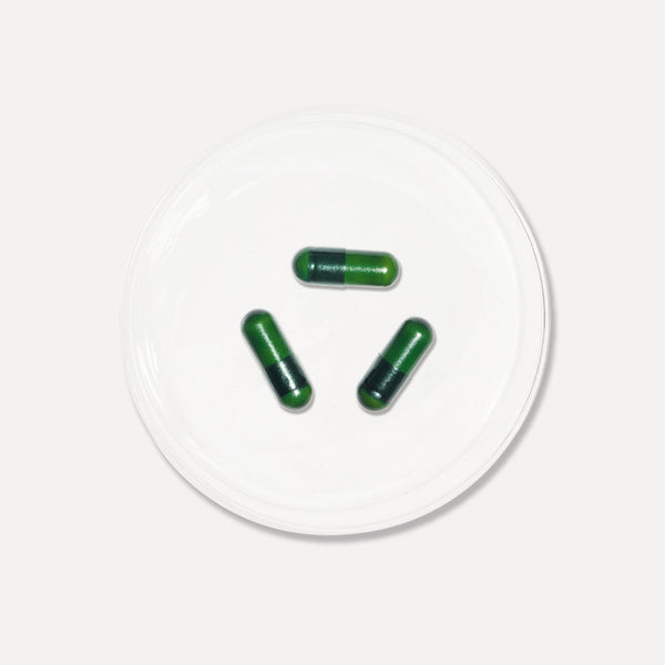 Three green capsules on a white circular platform with a white background