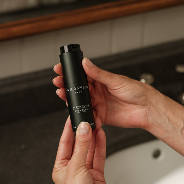 Hand holding a black skincare product labeled 'Wildsmith' in a bathroom setting.