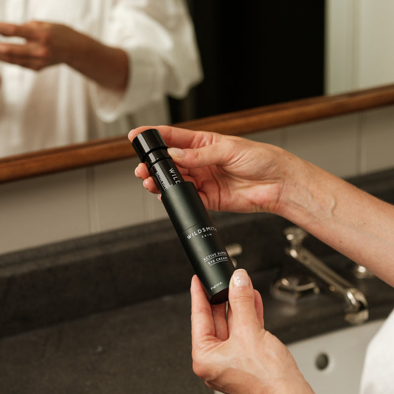 Person holding a black skincare bottle labeled 'Alvera' in front of a mirror.