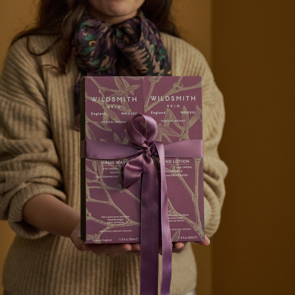 Person holding a Wildsmith hand care set with a purple ribbon against a warm-toned background