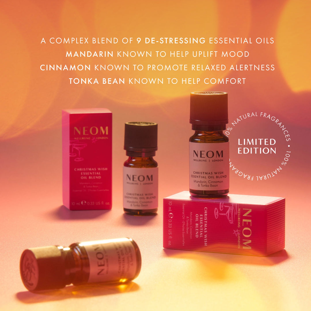 NEOM Christmas Warm Scents essential oil set featuring amber glass bottles, pink packaging boxes, and a rolled bottle on a warm orange gradient background with descriptive text overlays.