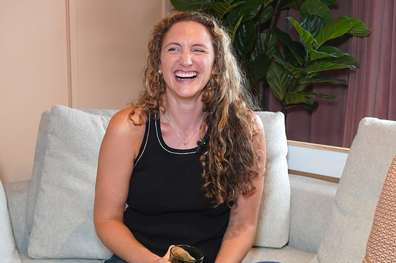 Woman sitting on a couch laughing with a plant in the background