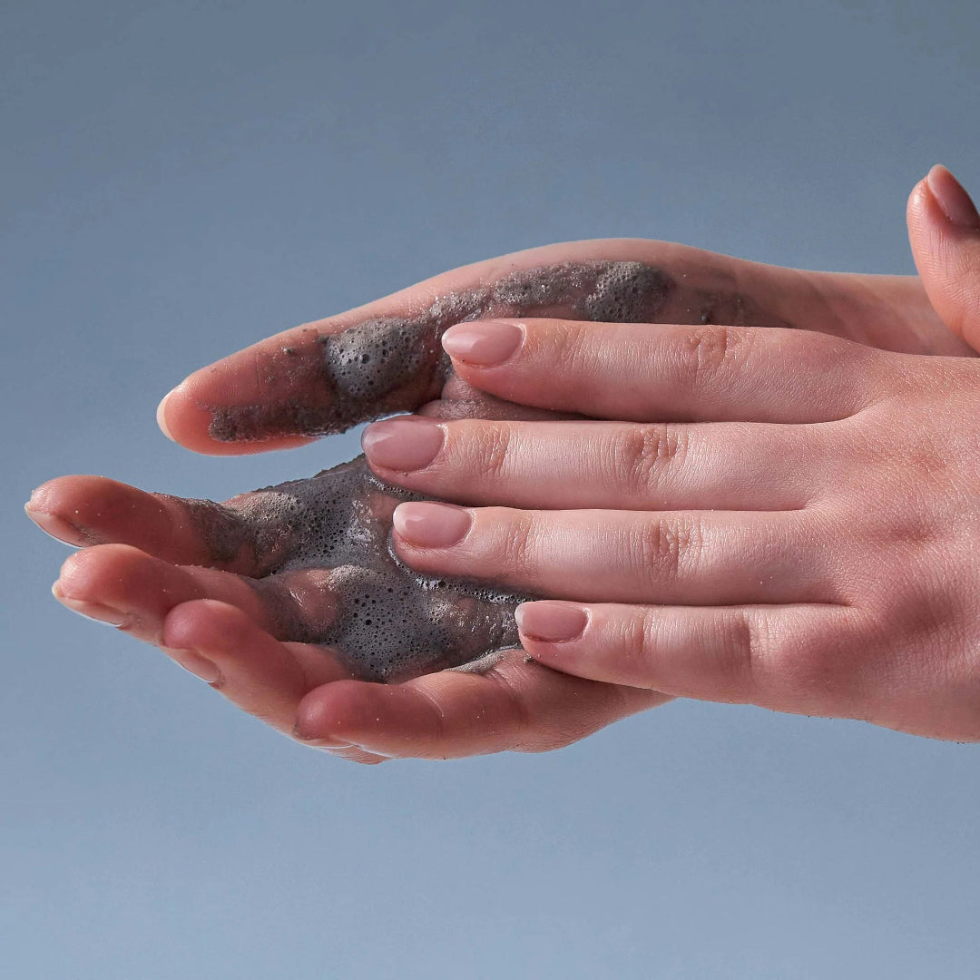 Hands holding a clump of dark gray clay against a light blue background