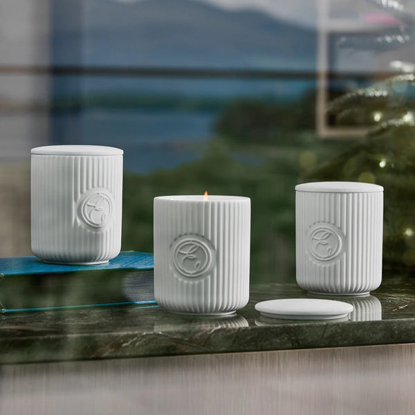 Three white textured candles on a reflective surface with a blurred natural background