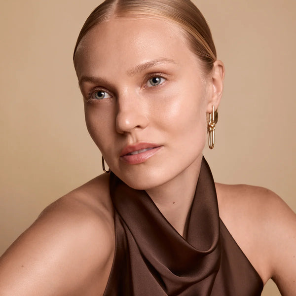 Woman wearing a brown top and gold hoop earrings against a beige background