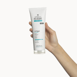 Hand holding a Heliocare UV Repair After Sun gel cream tube on a white background