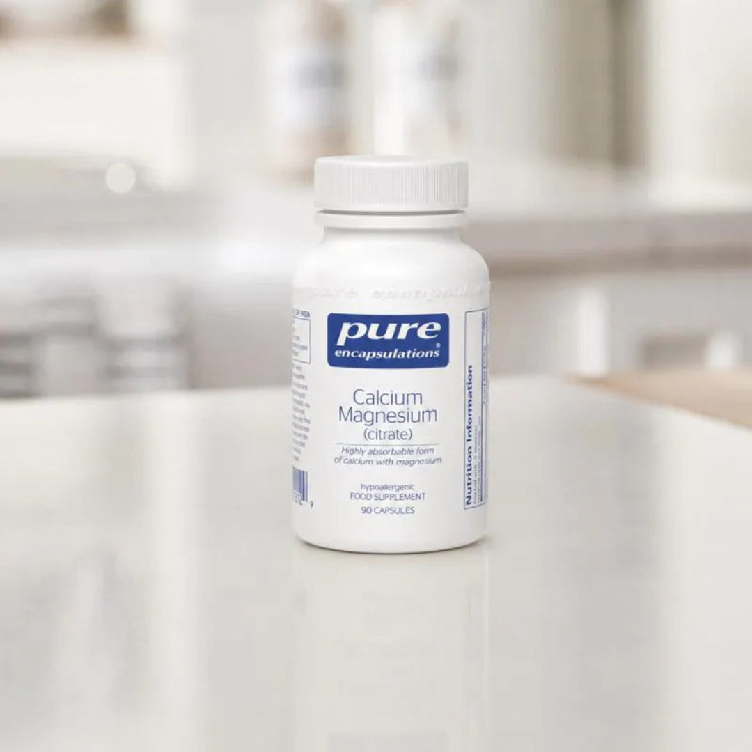 Bottle of Pure Encapsulations Calcium Magnesium supplement on a white surface with a blurred background